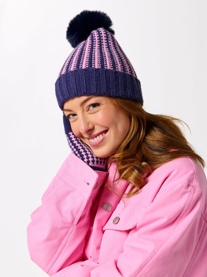 Person wearing a pink coat and striped beanie with a pom-pom on a white background