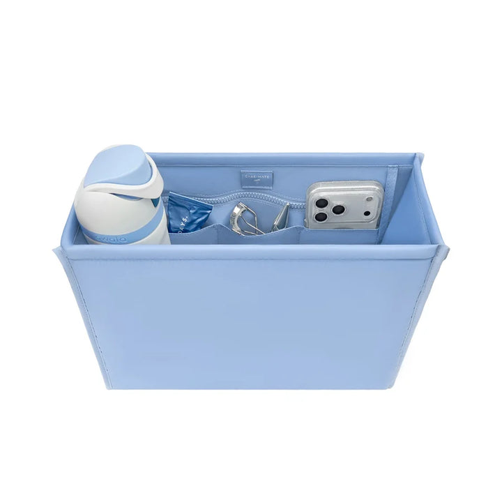 A light blue rectangular organizer tray with interior zippered compartments, shown holding a white and blue bottle, a small blue item, a silver ring, and a silver smartphone. The organizer is photographed on a clean white background.