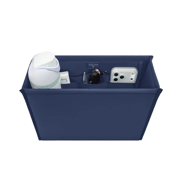 A navy blue fabric organizer bin with multiple compartments, shown holding various items including a white bottle, a small jar, sunglasses, and a smartphone case, on a solid white background.