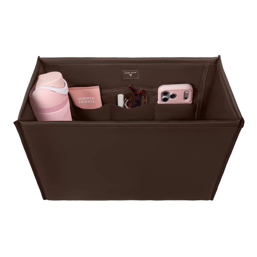 A brown fabric organizer bag with multiple compartments, shown from a top-down view on a white background. The organizer is styled with various pink and white items, including a water bottle, a phone case, and a small card holder.