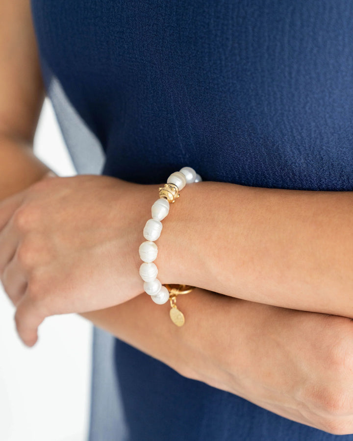 Pearl bracelet with gold accents on a wrist against a blue background
