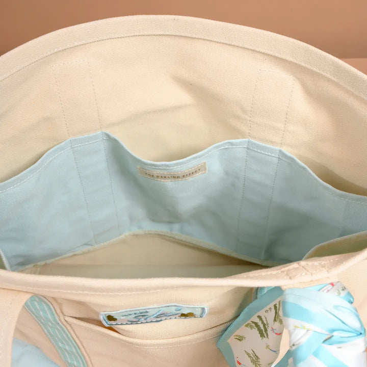 Close-up of the interior of a cream canvas tote bag with a light blue fabric organizer insert and a small printed brand label.