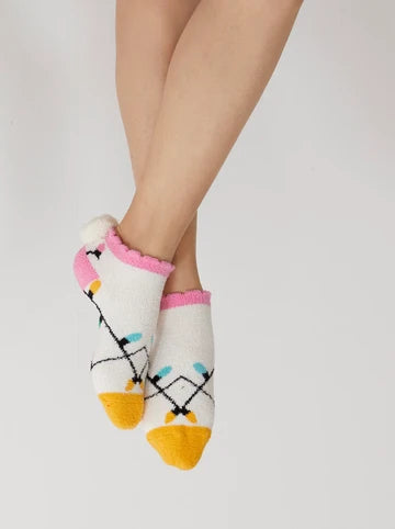 A pair of low-cut socks worn on a person's feet, featuring a white base with a colorful Christmas string lights pattern, pink ruffled trim, and yellow toes, set against a plain light gray background.
