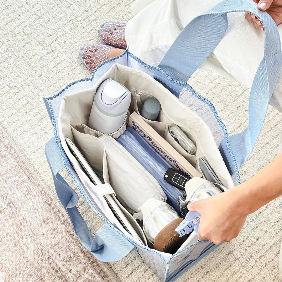 A light blue and white patterned diaper bag organizer filled with baby items, shown on a textured beige rug with a person&