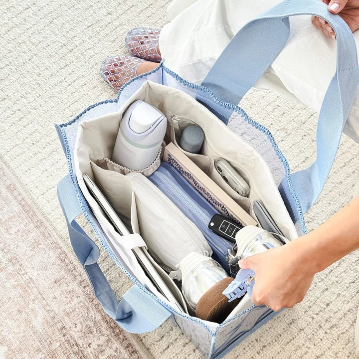 A light blue and white patterned diaper bag organizer filled with baby items, shown on a textured beige rug with a person&
