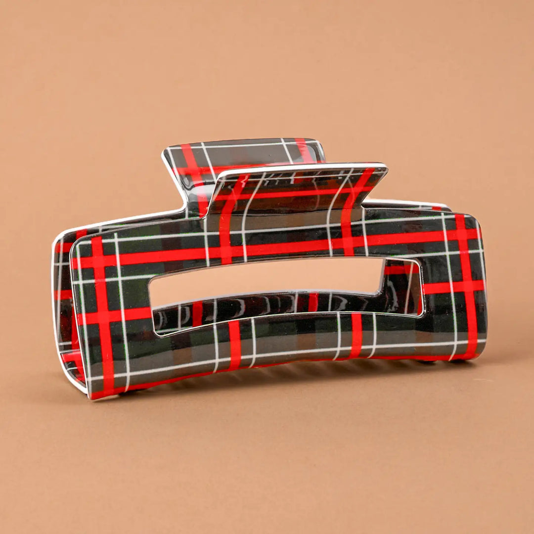 A glossy hair claw clip with a red, black, and white plaid pattern, shown on a solid tan background.