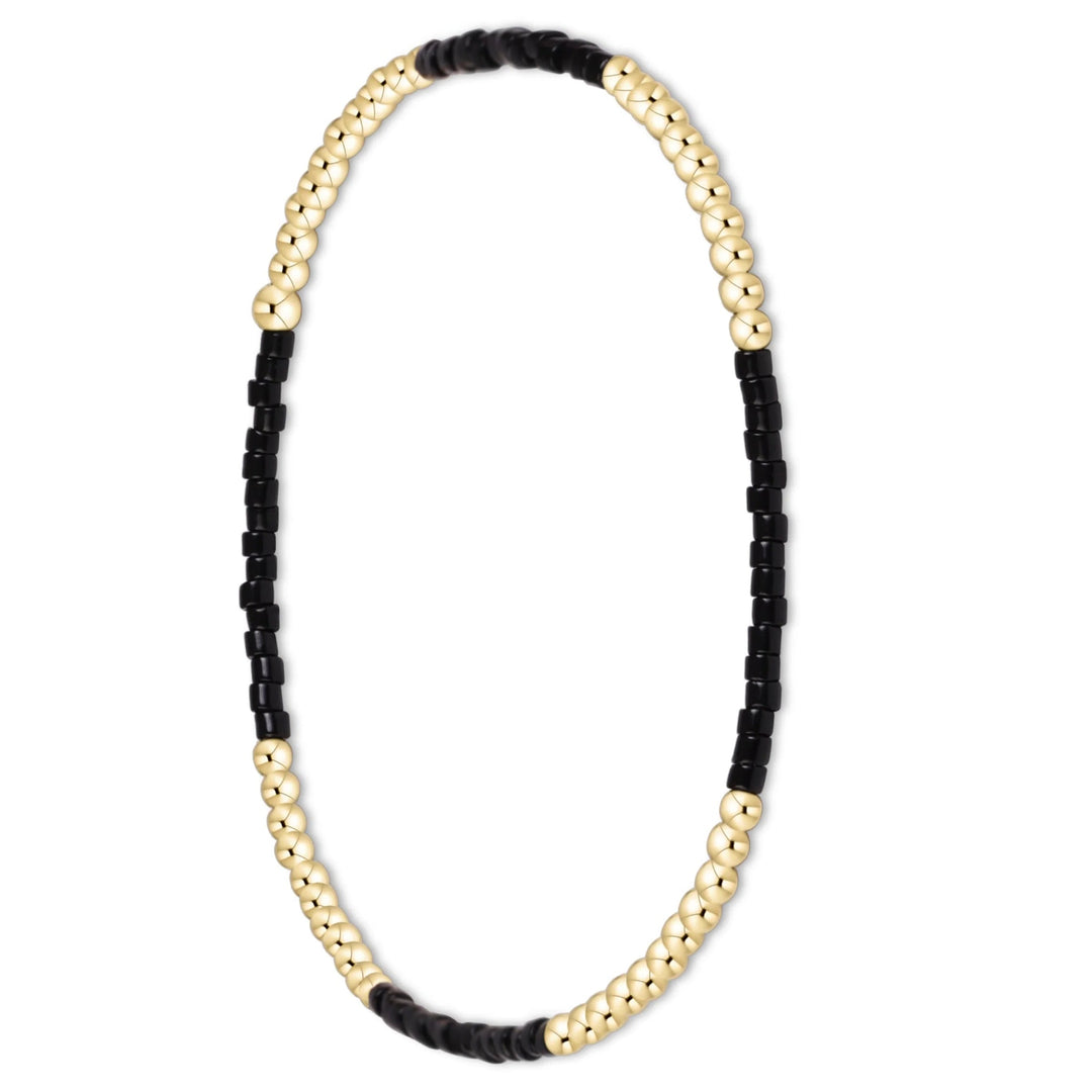 A beaded stretch bracelet featuring alternating sections of polished gold-tone round beads and matte black cylindrical beads, displayed on a clean white background.