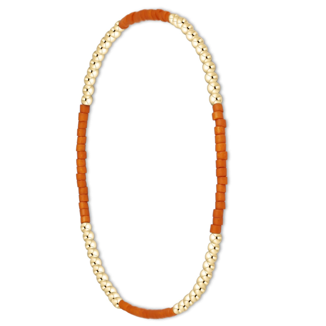 A beaded stretch bracelet featuring alternating strands of small metallic gold beads and textured orange cylindrical beads, shown against a plain white background.