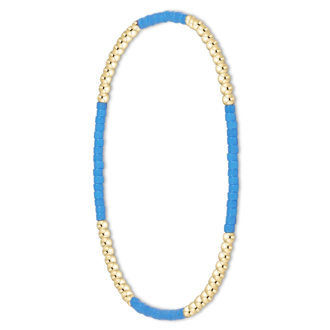 A beaded stretch bracelet featuring alternating rows of small metallic gold beads and bright blue cylindrical beads, displayed on a clean white background.