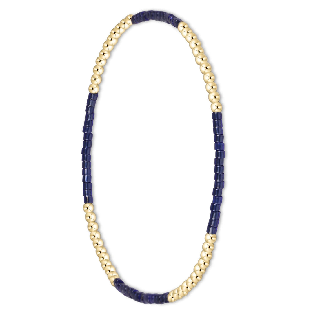 A beaded stretch bracelet featuring alternating strands of polished gold-toned round beads and dark navy blue rectangular beads, displayed on a clean white background.