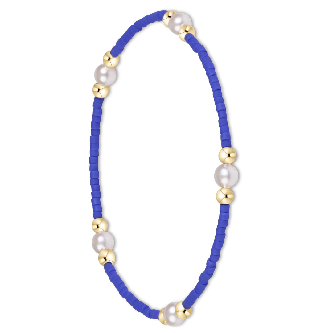 A delicate beaded bracelet featuring vibrant royal blue cylindrical beads, accented with white freshwater pearls and polished gold spacer beads, shown on a clean white background.