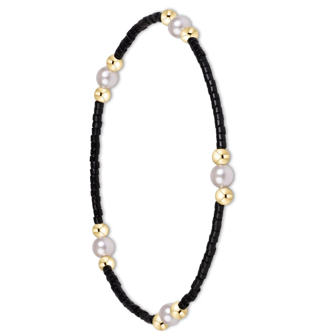 A delicate beaded bracelet featuring a black bead chain accented with large white pearls and polished gold spacer beads, displayed on a clean white background.
