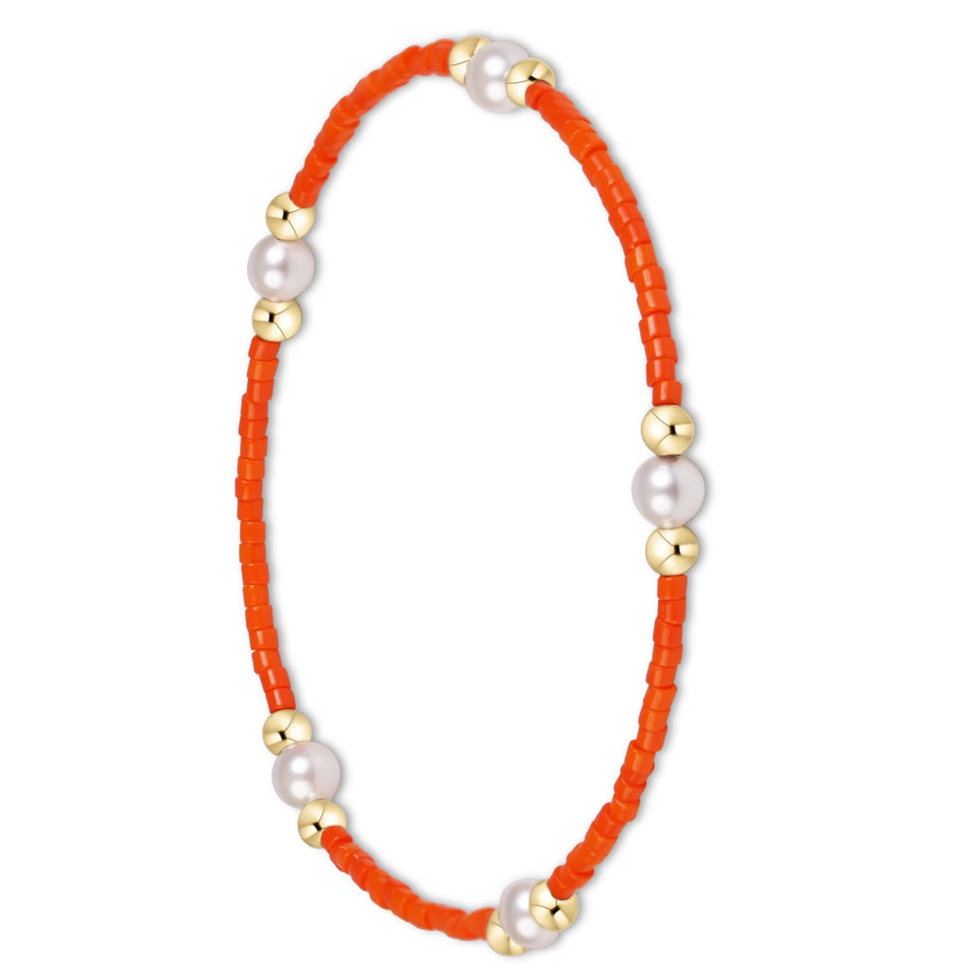 A beaded bracelet featuring vibrant orange cylindrical beads, white pearl-like round beads, and small gold spacer beads, arranged in a circular loop on a plain white background.