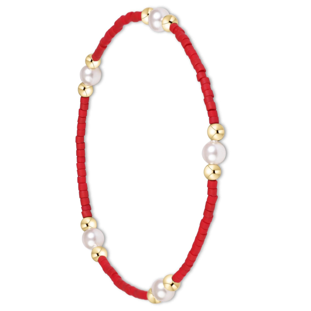 A red beaded cord bracelet with white pearls and gold spacer beads, arranged in an oval shape on a plain white background.
