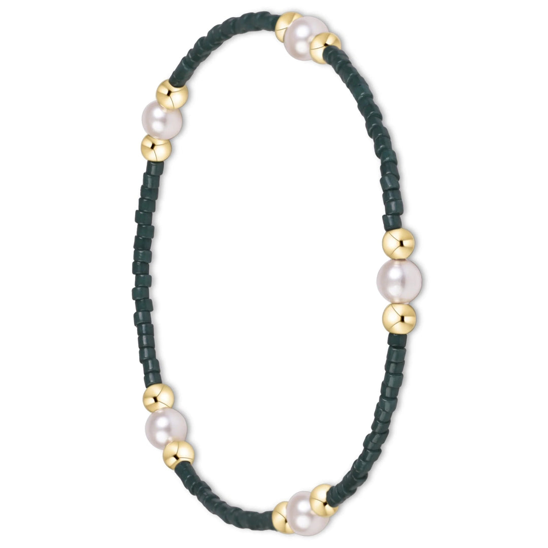 A delicate beaded bracelet featuring dark green faceted beads, white freshwater pearls, and polished gold spacer beads, arranged in a circular shape on a plain white background.