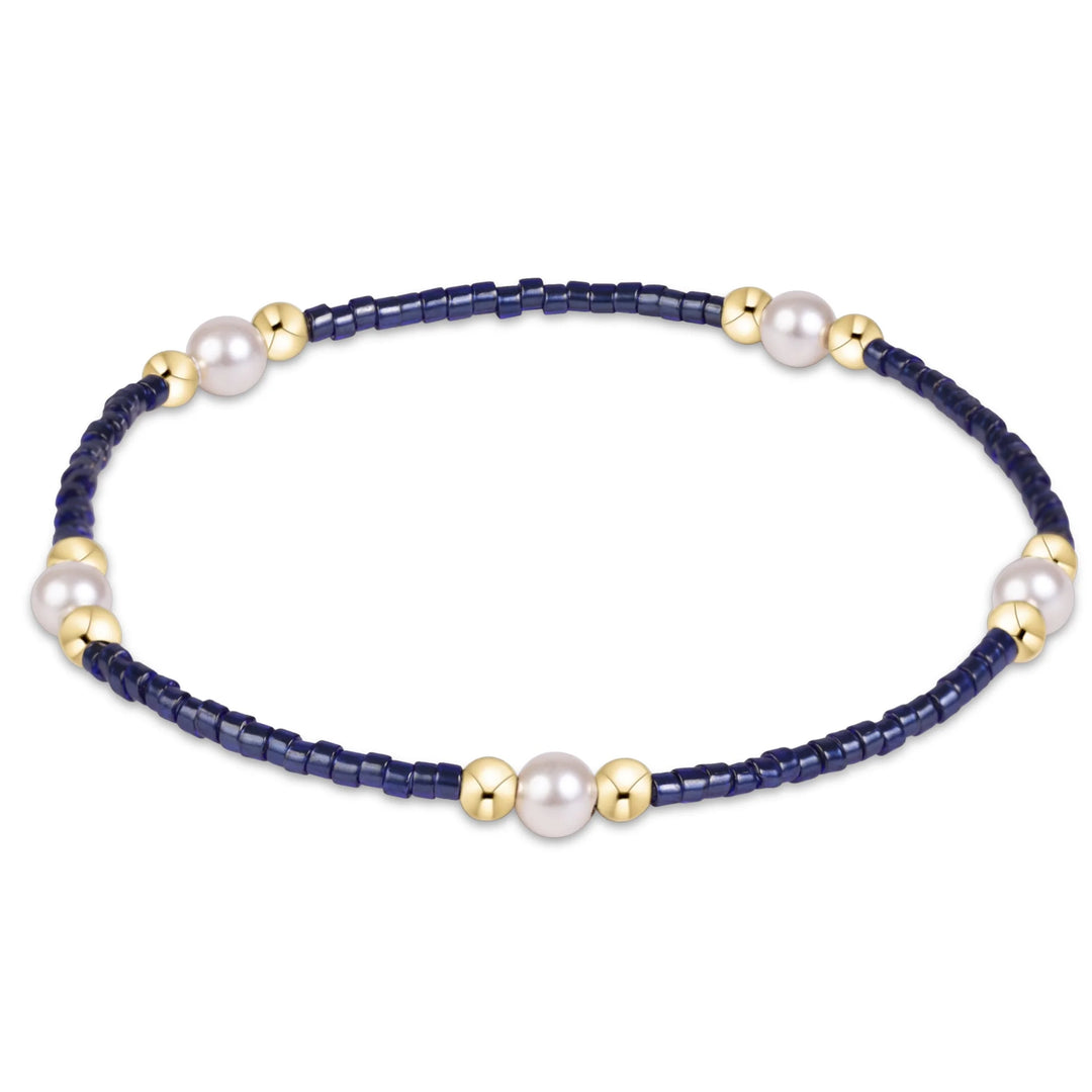 A delicate beaded bracelet featuring dark navy blue faceted beads, large white freshwater pearls, and polished gold spacer beads, displayed on a clean white background.