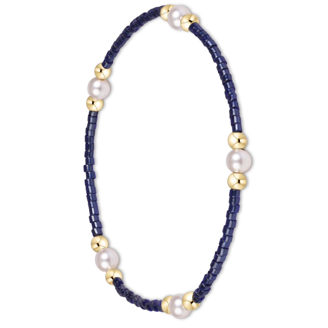 A delicate beaded bracelet featuring dark navy blue faceted beads, large white freshwater pearls, and polished gold spacer beads, displayed on a clean white background.