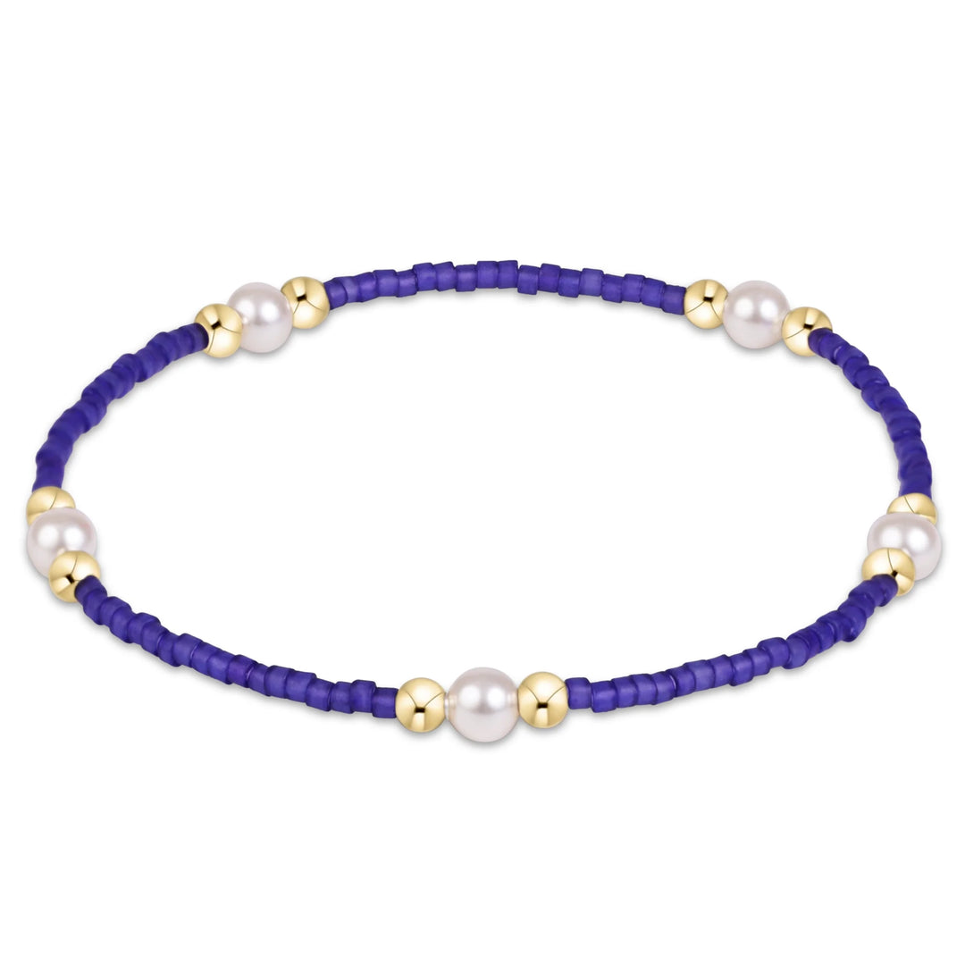 A beaded bracelet featuring a deep purple cord, white pearl-like beads, and small gold spacer beads, shown on a plain white background.