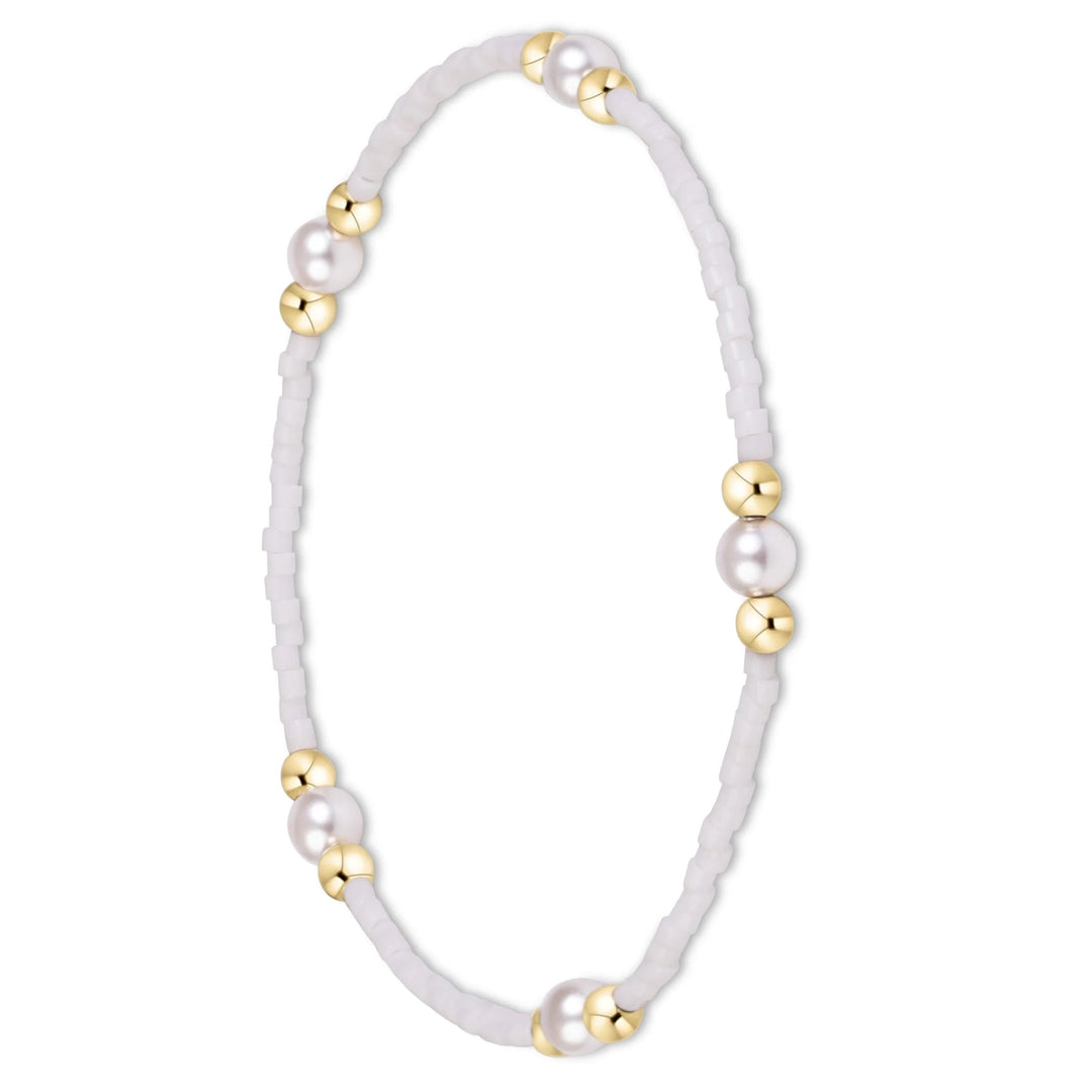 A delicate beaded bracelet with white faux pearls and polished gold spacer beads, arranged in a circle on a clean white background.