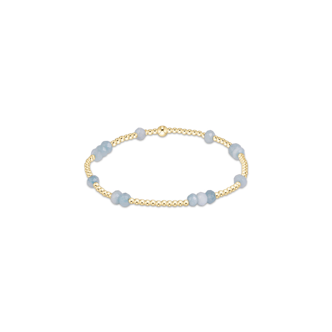 A delicate beaded bracelet featuring alternating strands of polished light blue faceted beads and gold-toned round beads, completed with a gold-toned clasp, shown on a plain white background.