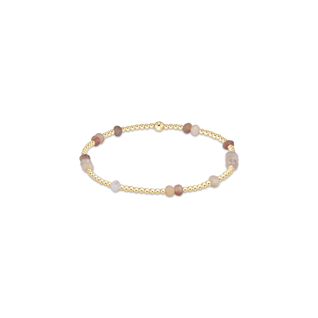 A delicate beaded stretch bracelet featuring gold-plated round beads interspersed with smooth, polished stone beads in soft shades of brown, beige, and pale lavender, displayed on a clean white background.