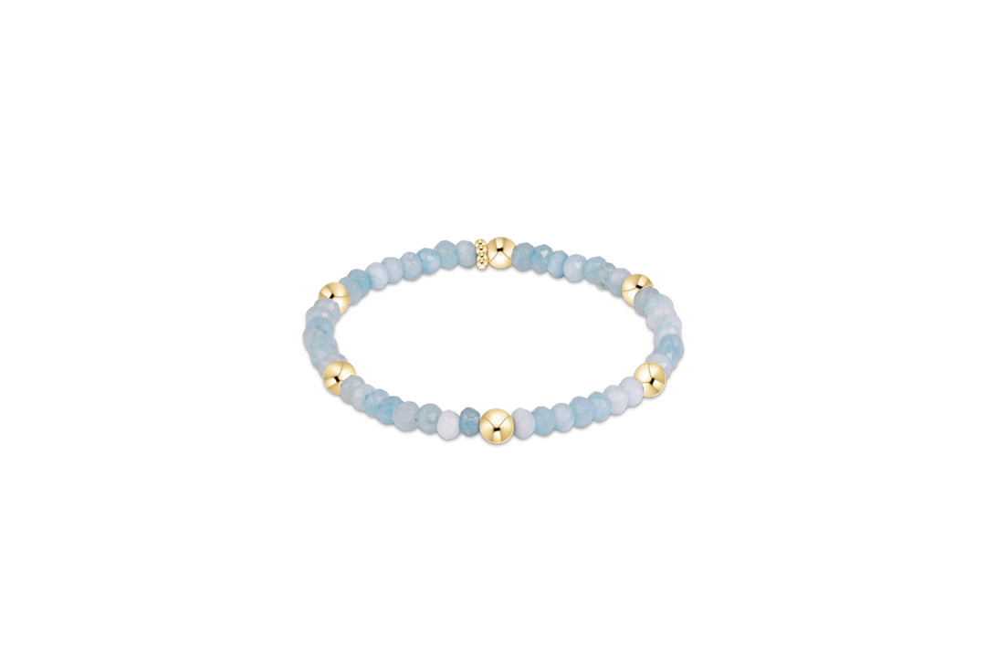A beaded stretch bracelet featuring light blue and white stones with polished gold spacer beads, displayed on a clean white background.