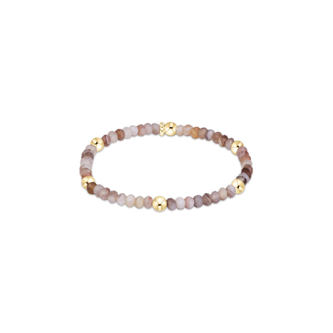 A beaded stretch bracelet featuring faceted natural stone beads in shades of brown, beige, and lavender, accented by polished gold-tone metal beads and a clasp, shown on a plain white background.