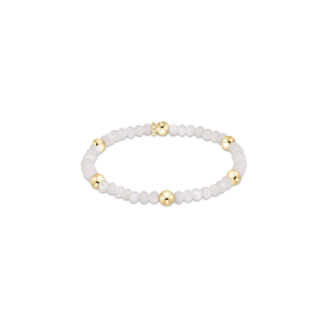 A beaded stretch bracelet featuring white marbled round beads and polished gold spacer beads, displayed on a clean white background.