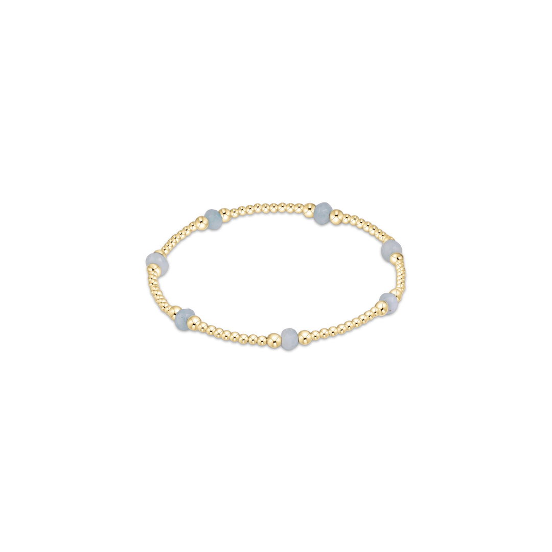 A gold beaded stretch bracelet featuring alternating smooth, light blue-gray round beads and polished gold spacer beads, shown on a plain white background.