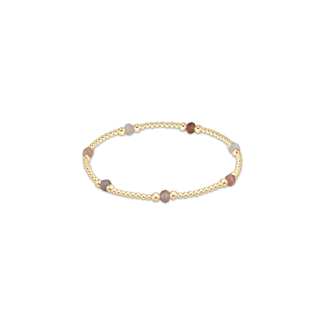 A gold beaded stretch bracelet with alternating smooth round beads in soft pink, gray, and reddish-brown tones, displayed on a clean white background.