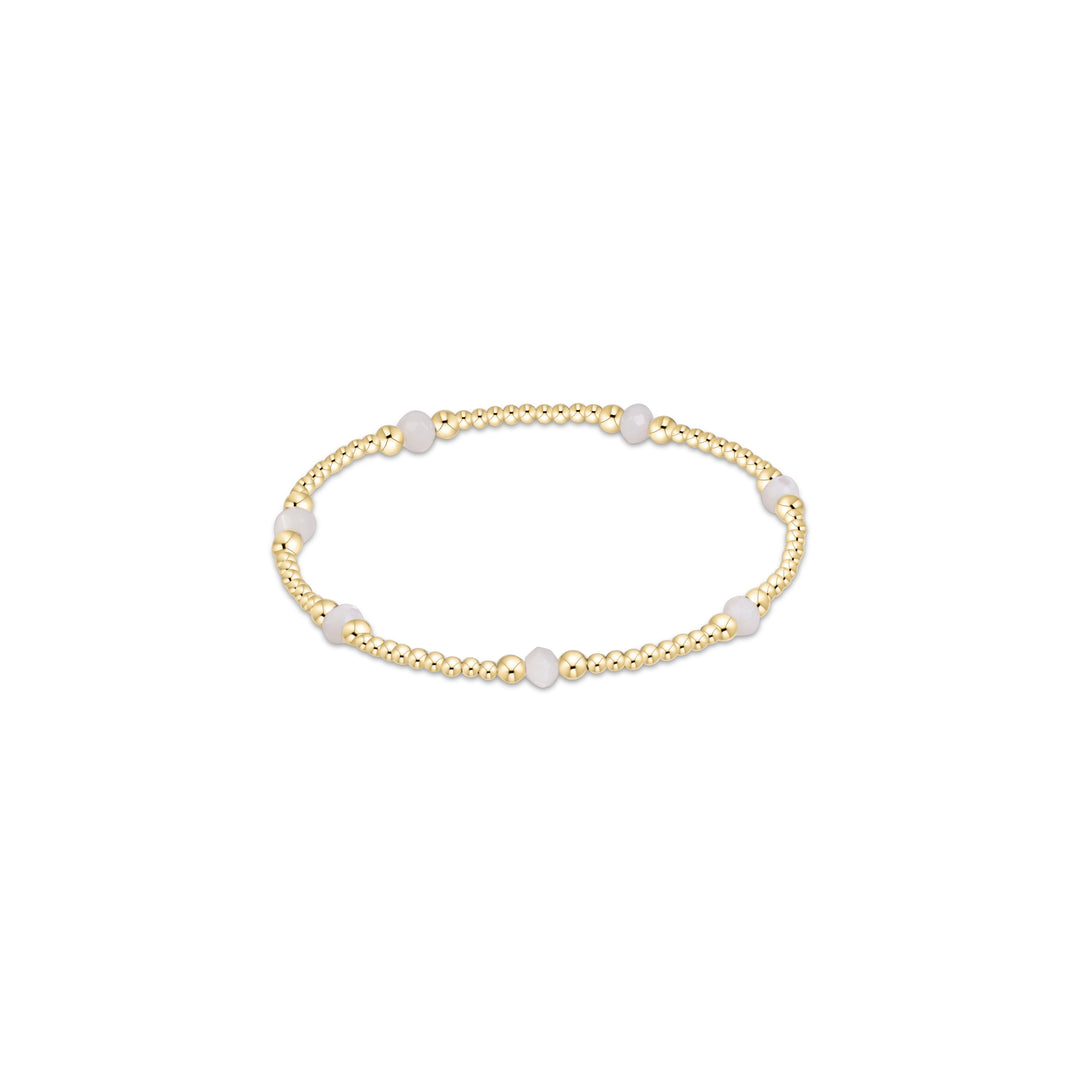 A delicate gold beaded stretch bracelet featuring alternating smooth white oval beads and polished round gold beads, displayed on a clean white background.