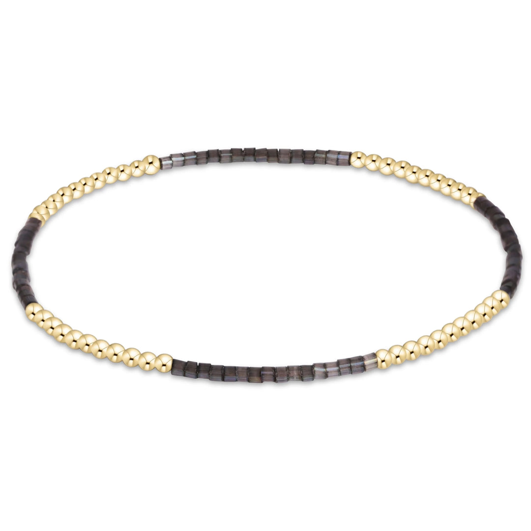 A beaded stretch bracelet featuring alternating sections of polished gold-toned beads and dark gray faceted stone beads, displayed on a clean white background.