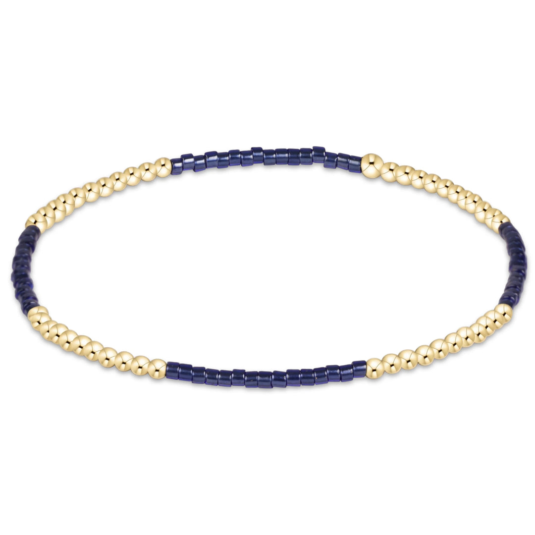 A delicate beaded bracelet featuring alternating sections of polished gold-toned round beads and dark navy blue cylindrical beads, displayed on a clean white background.
