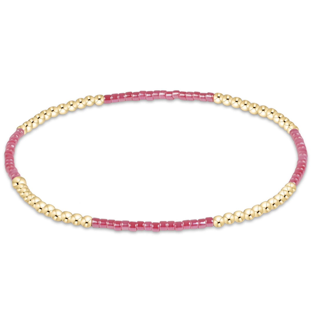 A delicate beaded stretch bracelet featuring alternating sections of polished gold-tone beads and translucent pink cylindrical beads, displayed on a clean white background.