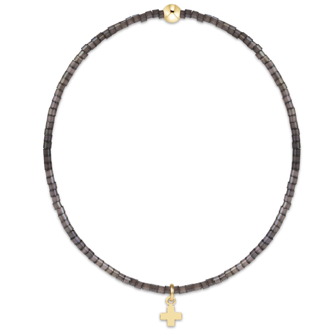 A beaded necklace featuring dark gray square beads and a small gold cross pendant, displayed on a clean white background.
