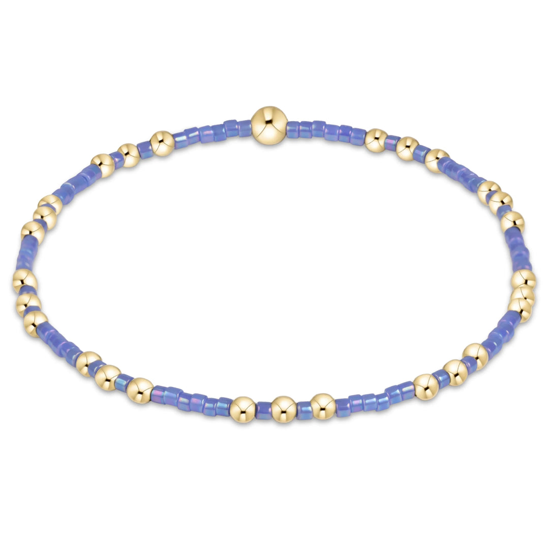 A beaded stretch bracelet featuring light blue translucent square beads and polished gold-tone round beads, with a central gold clasp, shown on a plain white background.