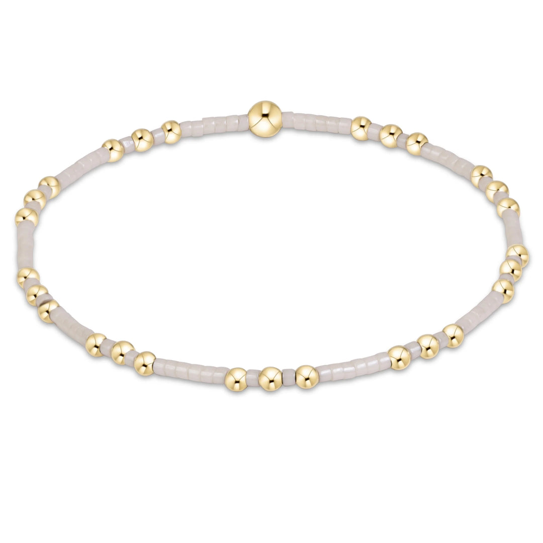 A delicate beaded stretch bracelet featuring light gray translucent beads and polished gold-tone spacer beads, displayed on a clean white background.