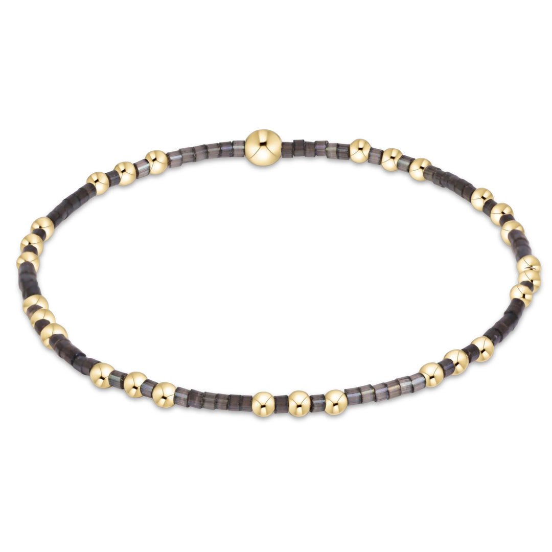 A beaded stretch bracelet featuring alternating polished gold-tone beads and dark gray faceted beads, with a larger central gold bead and a matching gold clasp, shown on a plain white background.