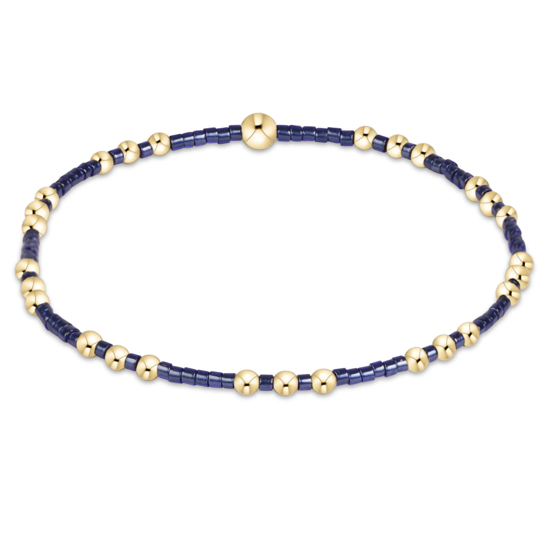 A beaded stretch bracelet featuring dark navy blue cylindrical beads and polished gold spherical beads, displayed on a clean white background.