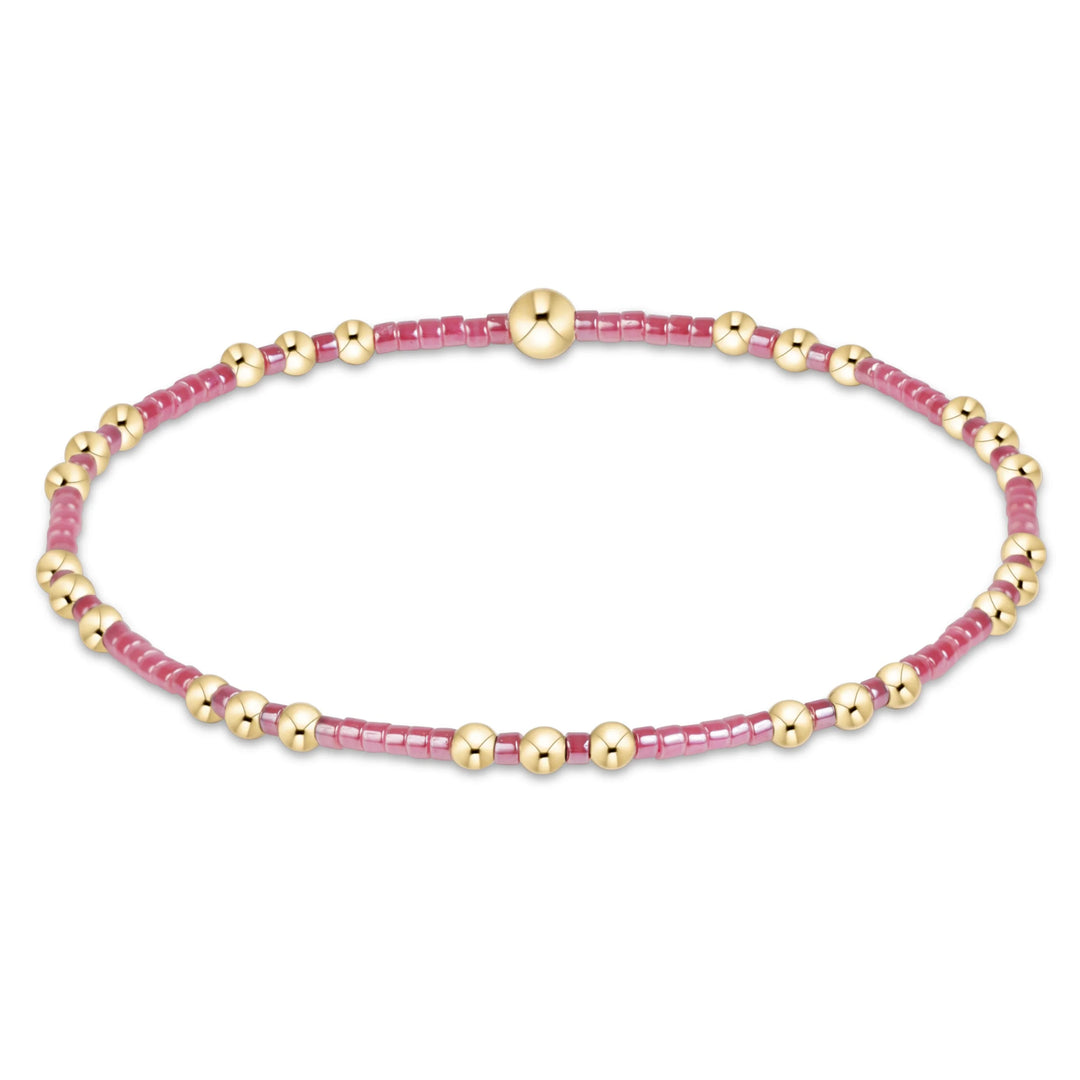 A delicate beaded bracelet with small pink faceted beads and polished gold spacer beads, arranged in an oval shape on a plain white background.