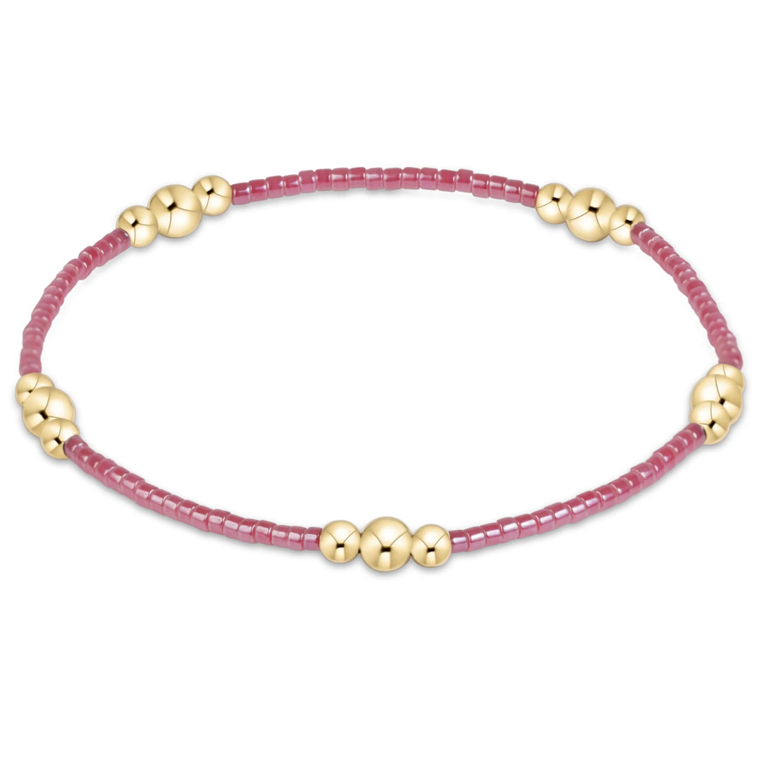 A delicate beaded bracelet with small faceted pinkish-red beads and five polished gold-toned spacer beads, displayed on a clean white background.