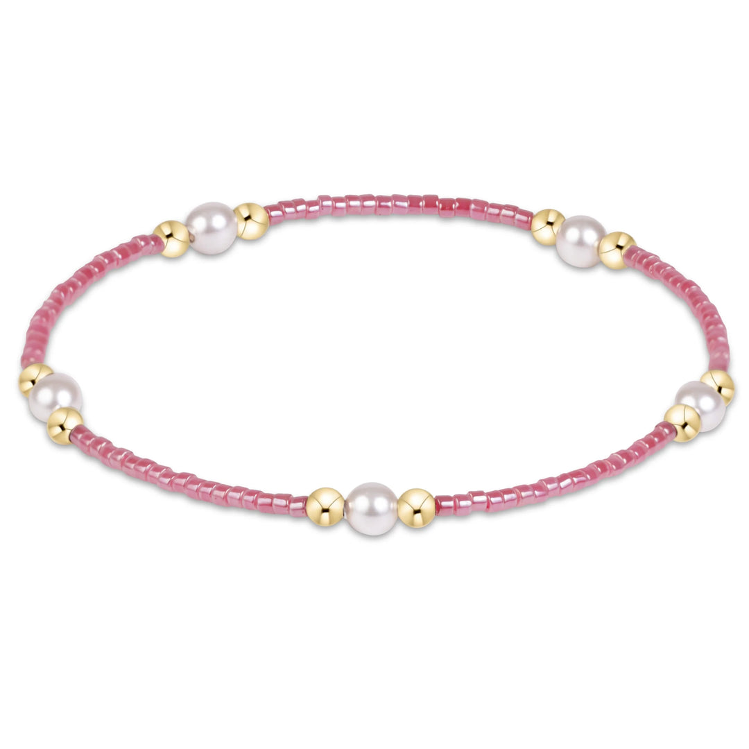 A delicate beaded bracelet featuring pink faceted beads, white pearl-like beads, and polished gold spacer beads, arranged in a horizontal oval on a clean white background.