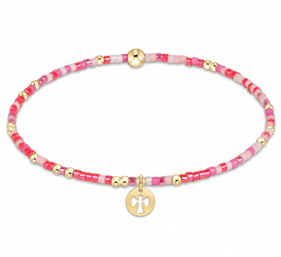 A delicate beaded bracelet with pink and white beads, accented by small gold spacer beads and a gold circular charm featuring a white cross, shown on a plain white background.