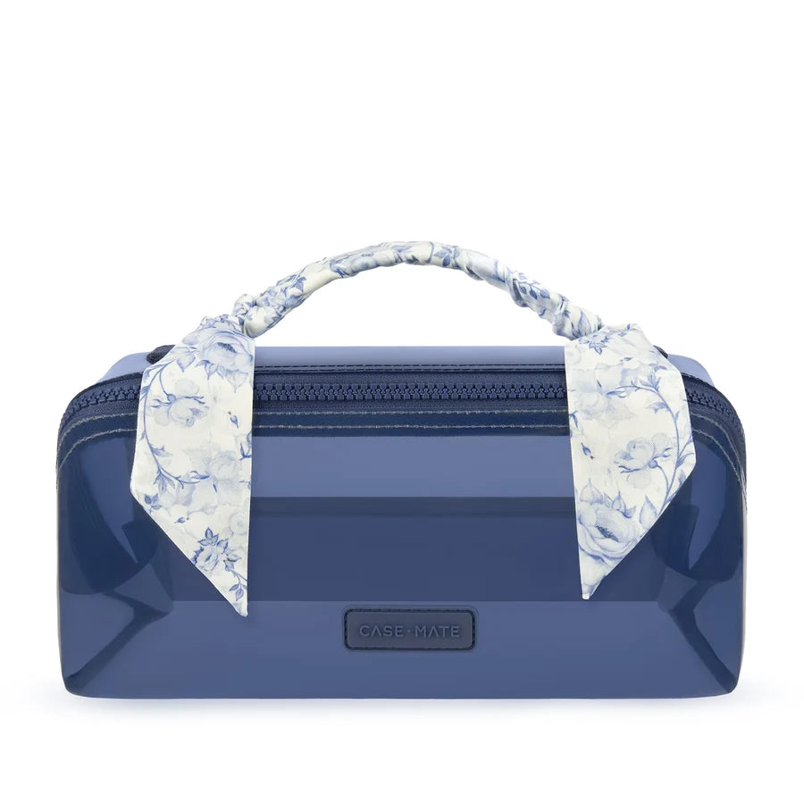 A glossy navy blue cosmetic case with a top zipper, a matching fabric handle, and a blue-and-white floral scarf tied to the handle. A small black CASE-NATE logo plaque is centered on the front, set against a plain white background.