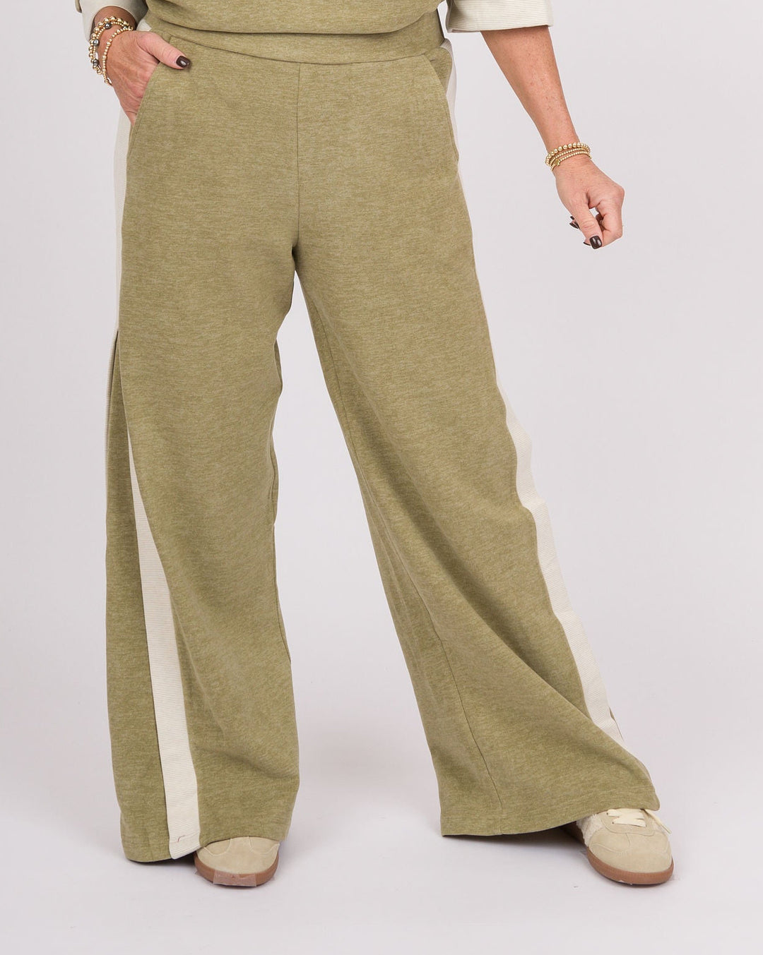 A woman modeling a matching two-piece lounge set consisting of a heathered sage green sweatshirt with white ribbed trim and matching wide-leg sweatpants with white side panels, photographed against a light gray studio background.