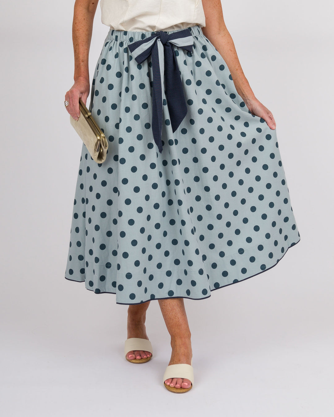 Person wearing a light blue polka dot skirt with a navy ribbon on a white background