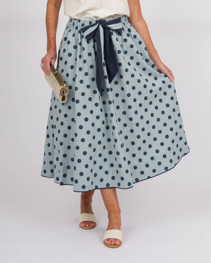 Person wearing a light blue polka dot skirt with a navy ribbon on a white background