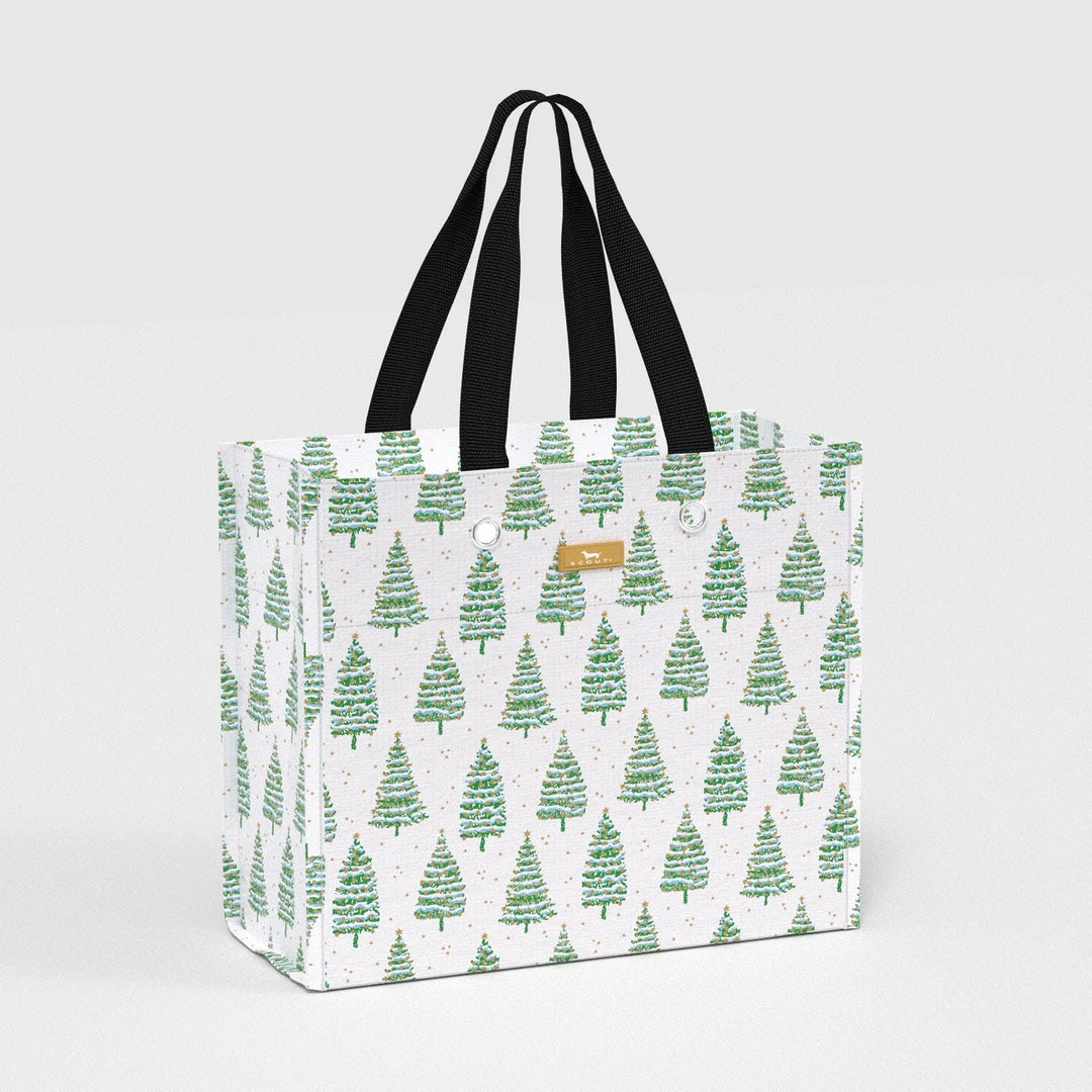 A white tote bag with a repeating green Christmas tree pattern, featuring black shoulder straps and a small tan leather brand patch that reads 'The Happy Bag'.