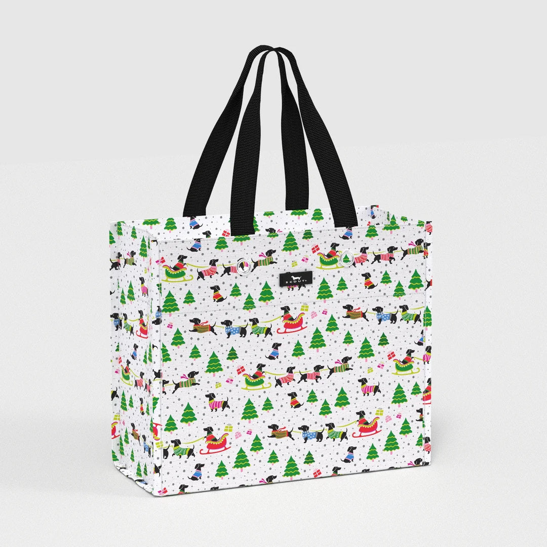 A white tote bag with black handles, featuring a festive Christmas print of black dogs in sleds, green Christmas trees, and small snowflakes on a light gray background.