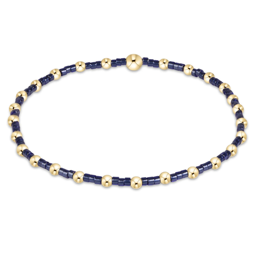 A beaded bracelet featuring dark navy blue cylindrical beads alternating with polished gold round beads, completed with a matching gold clasp, shown on a plain white background.